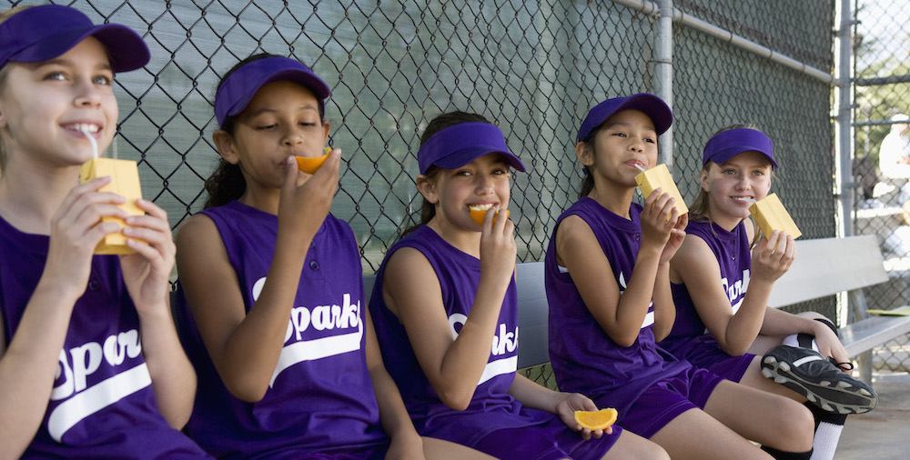 Little league players drinking juice boxes and eating snacks