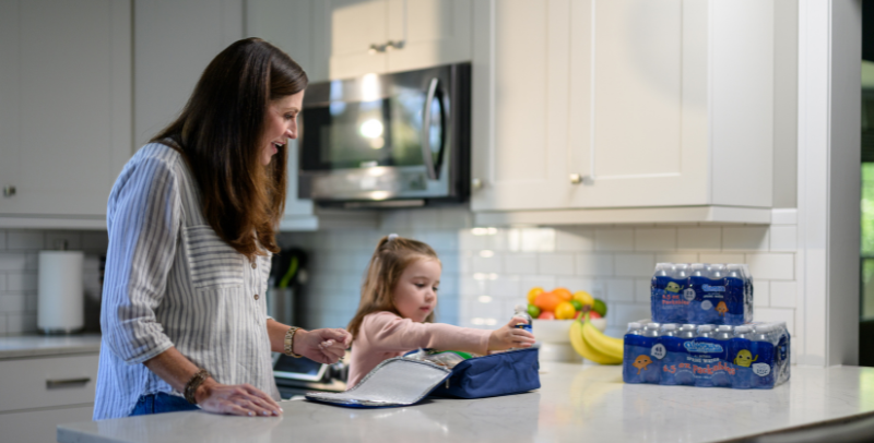 busy working mom helps young school age daughter pack her lunch bag with Absopure natural spring water